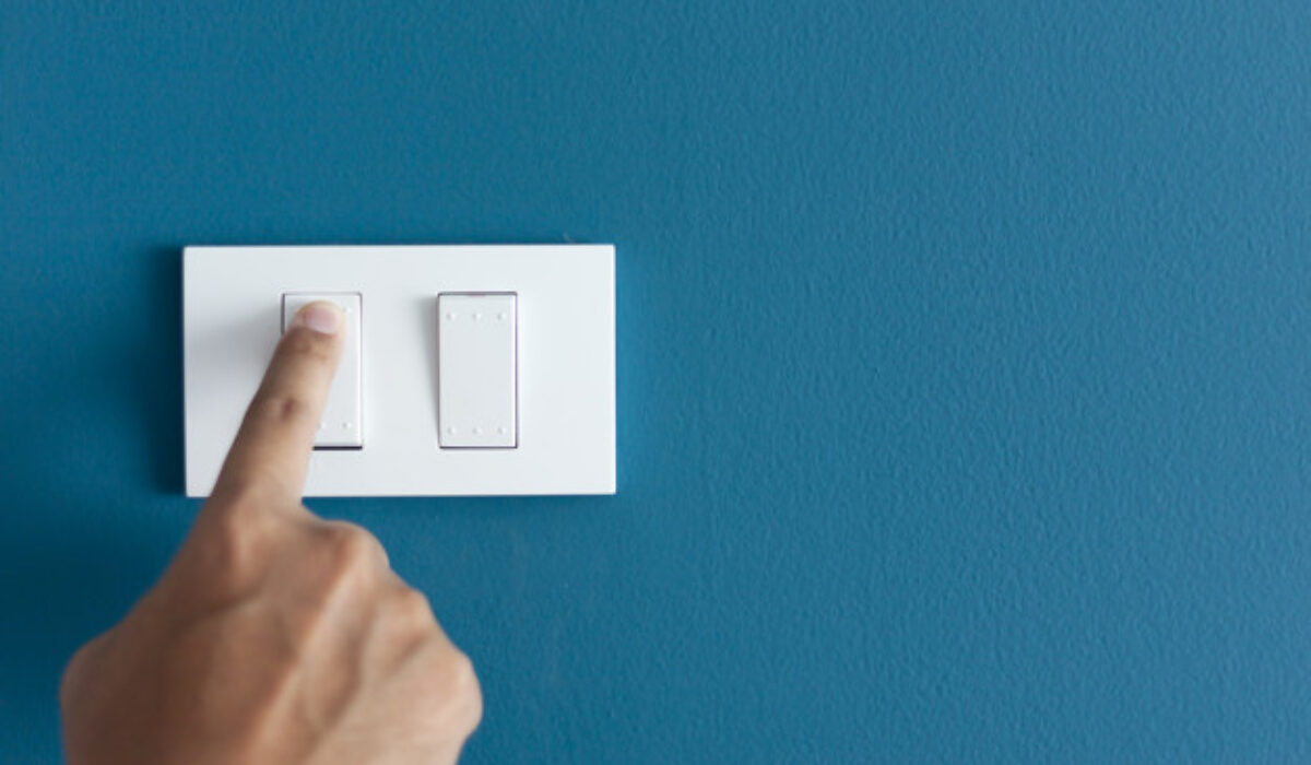 A finger turning on lighting switch on rough on blue dark wall. Empty space for text your